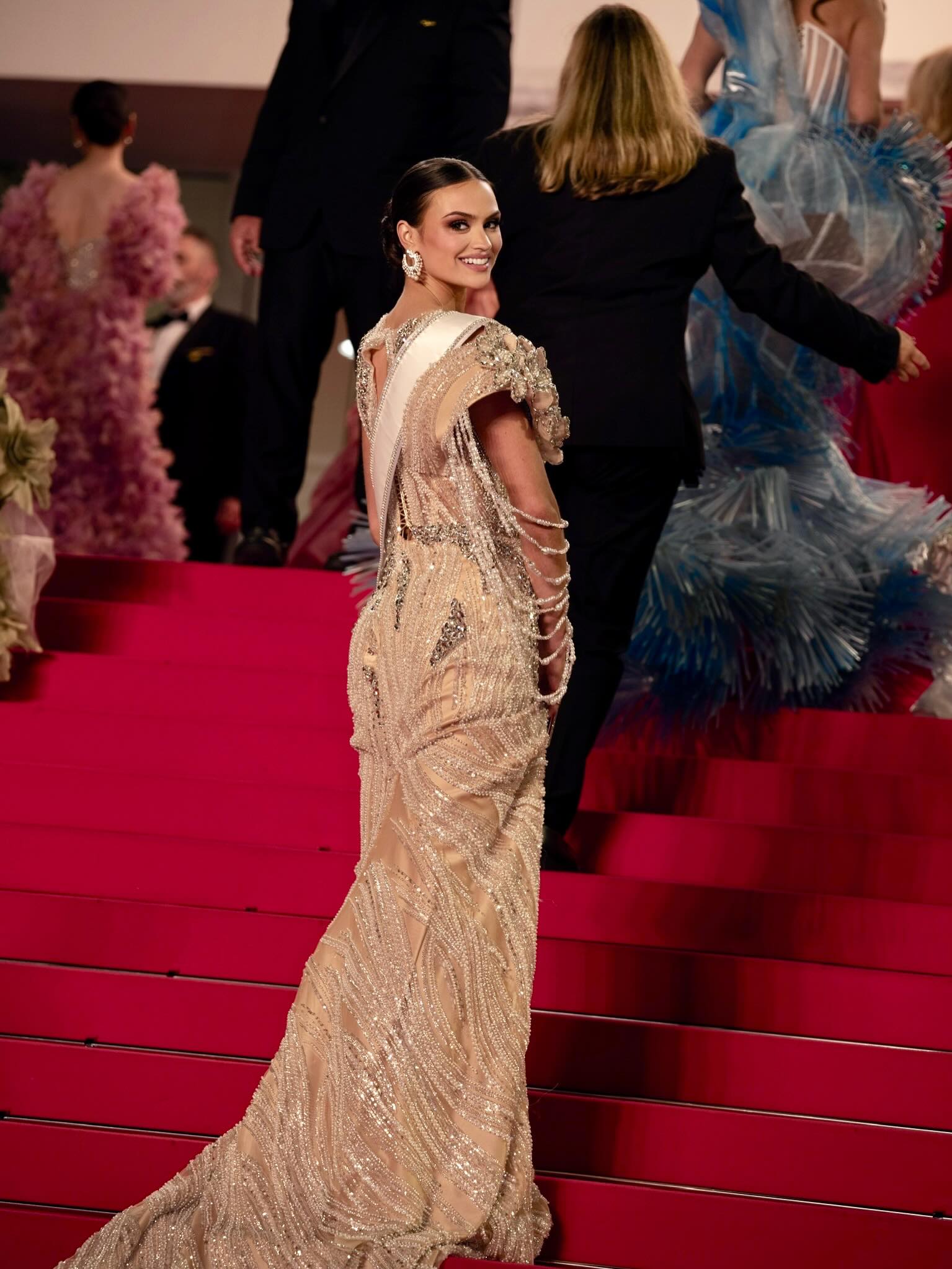 A contestant in a beaded champagne gown glances back over her shoulder on the red-carpet steps.