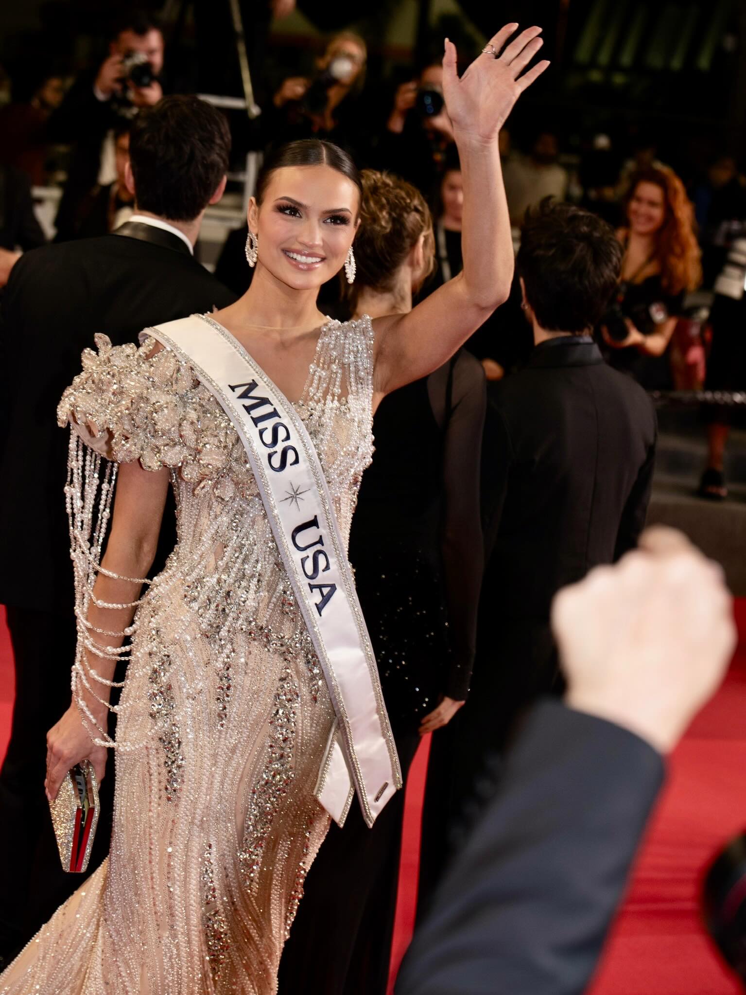 A contestant waves on the red carpet in a beaded gown with chandelier earrings and a slim clutch.